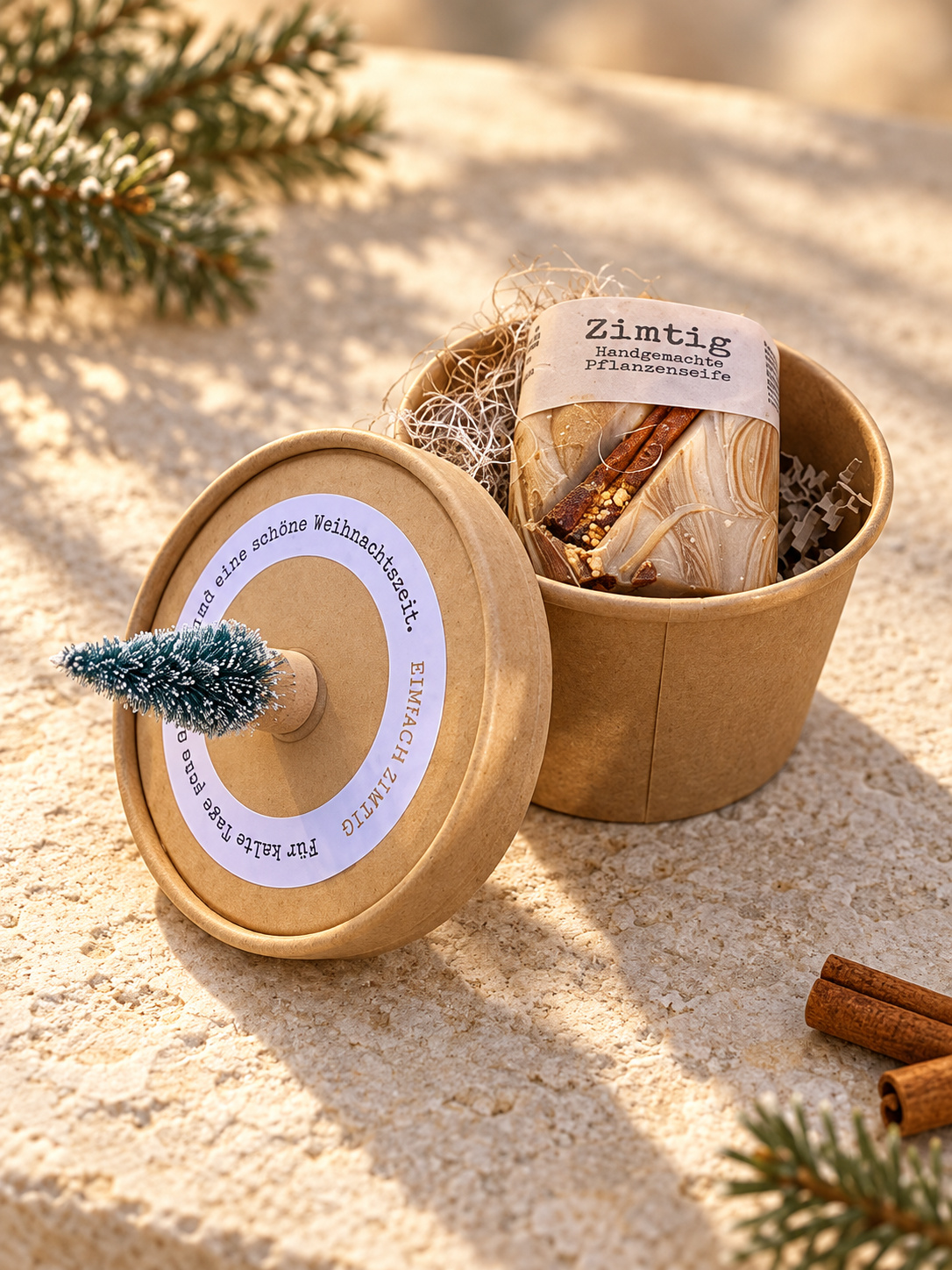 Geöffnete Geschenkbox „einfach Zimtig“ mit marmorierter Zimtseife und links angelehntem Deckel mit kleinem Tannenbäumchen im warmen Winterlicht.